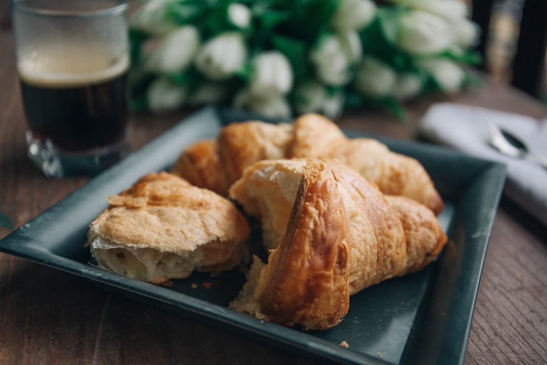 Picture shows a plate of croissants on a wooden table with a clear mug full of black coffee in the background 