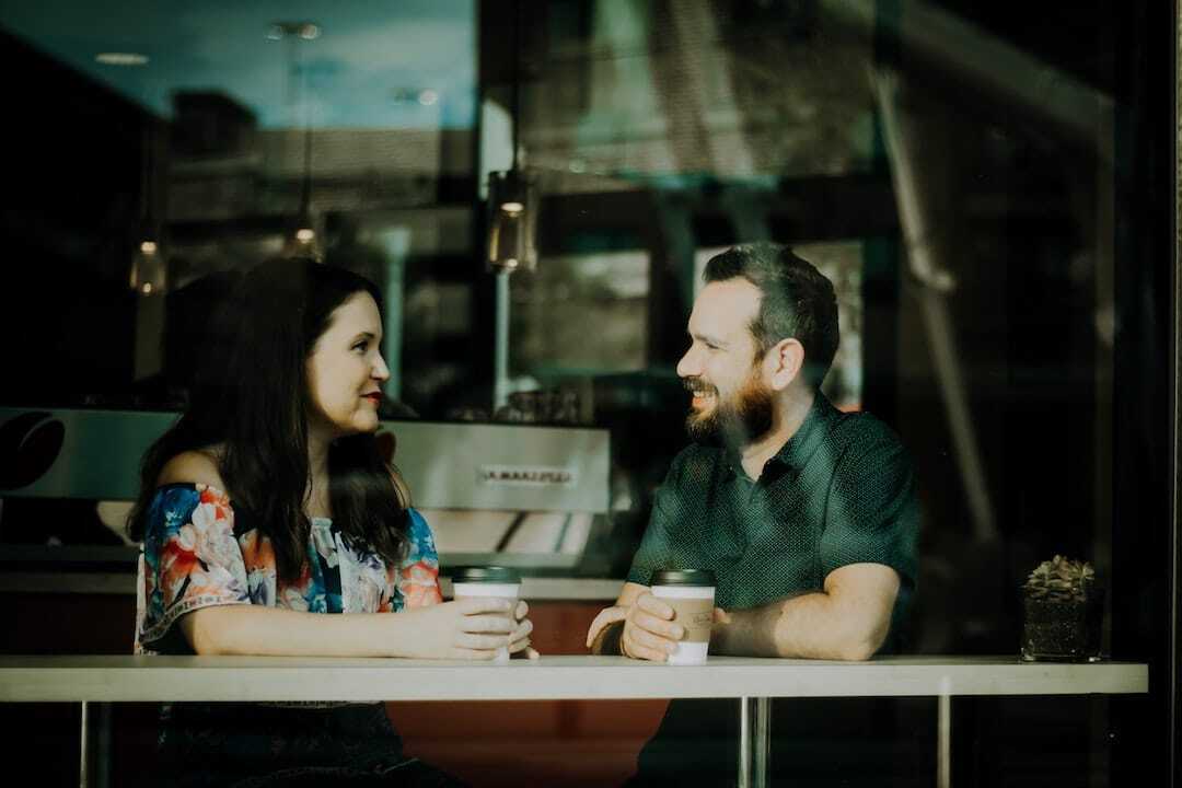 Image shows a man a a woman talking and drinking coffee