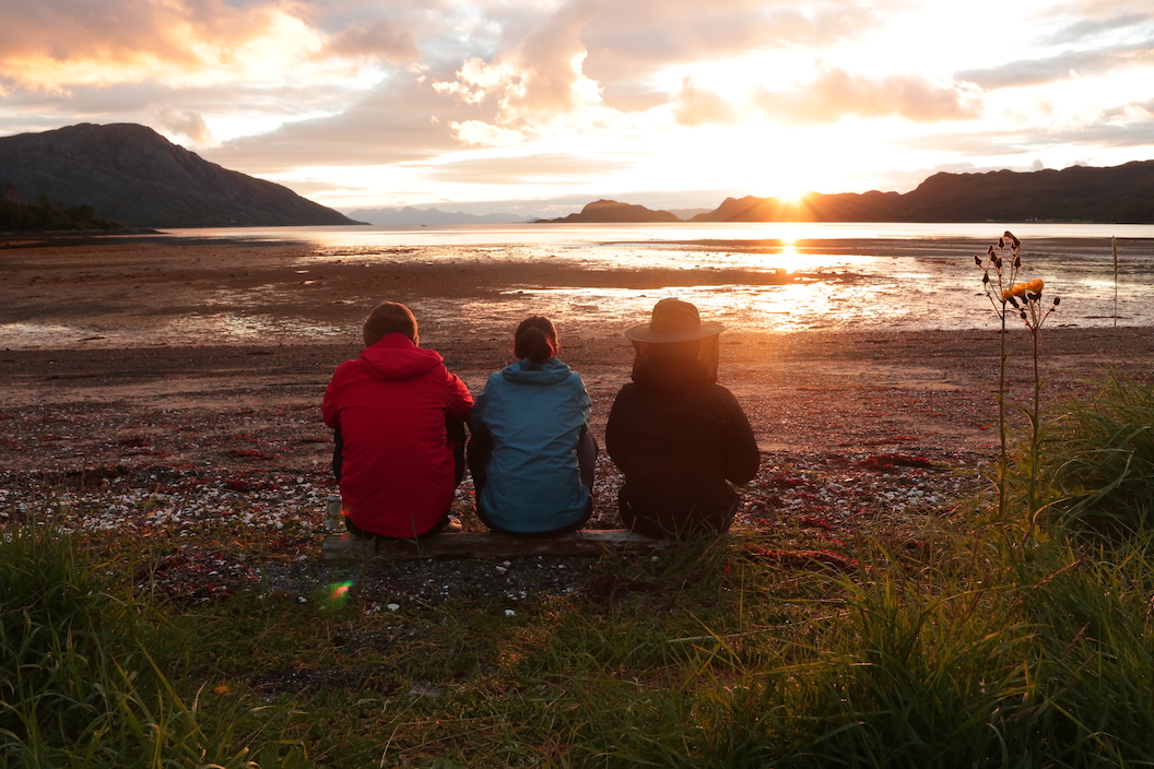 Image shows three friends on a beach looking out to sea