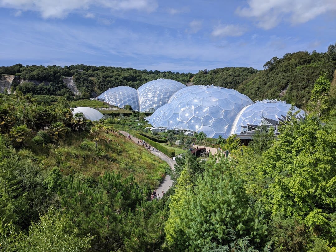 Image shows the Eden project in Cornwall. It is a bubble-like structure in the middle of lots of greenery