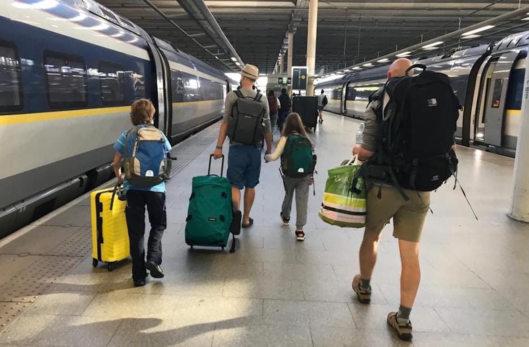 Image shows four people walking away from the camera, wheeling suitcases next to the Eurostar train
