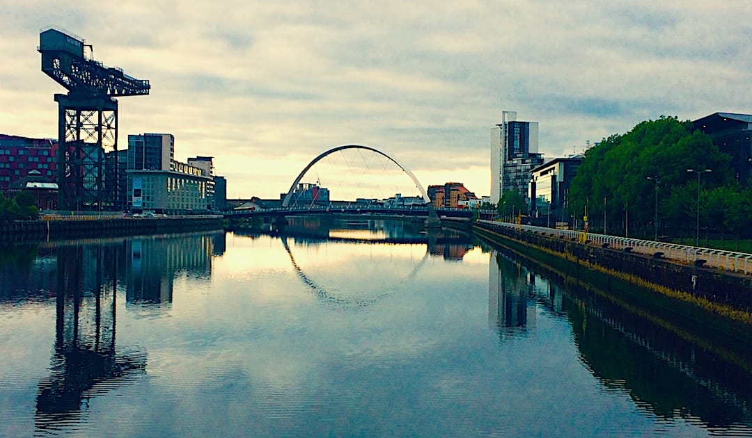 Image shows the river Clyde in Glasgow with an arch bridge going across, and industrial buildings on either side.