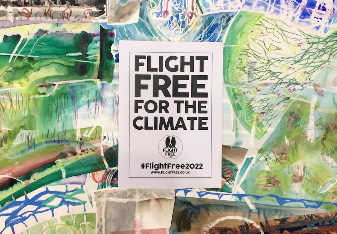 Image shows a flight free for the climate poster on top of a piece of abstract art, with lots of colours including green, blue and purple