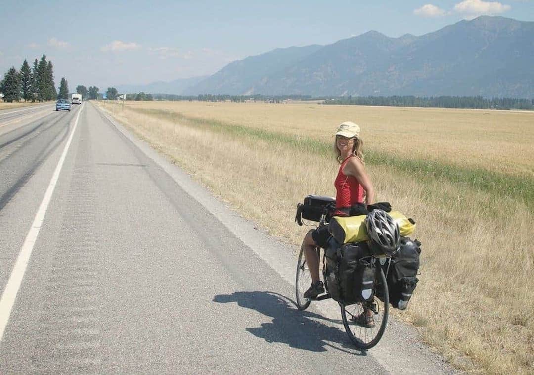 Picture shows Kate biking along a highway with mountains in the background