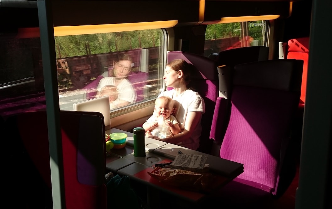 Picture shows Jennifer and Oren on the train from Scotland to Italy. Oren is sitting on Jennifers lap and sun is coming in from the train window. Jennifer is facing the sun with her eyes closed. 