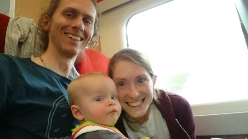 Picture shows Leo and Jennfier holding their baby Oren while sitting on a train. All three are looking at the camera and Leo and Jennifer are smiling. 