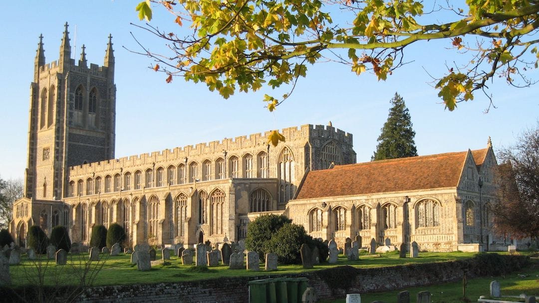 Image shows Long Melford church – a large church with a tower and a huge number of stained glass windows