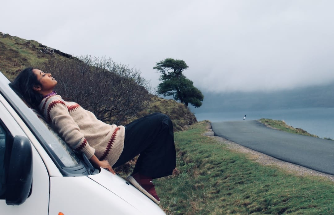 Sunita lies back on the windscreen of the van with a loch in the background and low white cloud